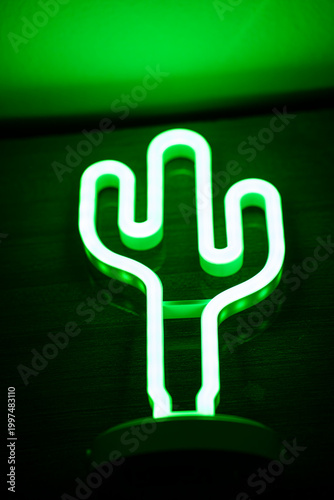 Green neon cactus lamp glowing in dark background.