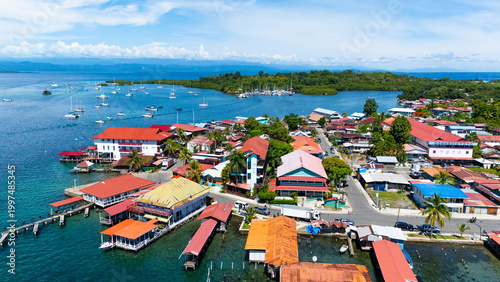Photos A stunning aerial drone view of Isla Colón showcasing crystal-clear turquoise waters, lush tropical vegetation, and colorful Caribbean-style buildings along the coastline