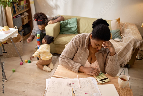 Foto Black mother calculating household expenses while children playing in living room, showing financial stress and poverty