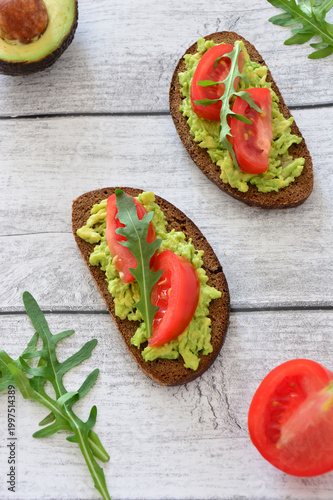 a vertical photo with Avocado Toast with Tomato and Arugula on Wooden Table