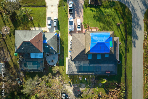 Hurricane Ian damaged house rooftop covered with protective plastic tarp against rain water leaking until replacement of asphalt shingles. Aftermath of natural disaster