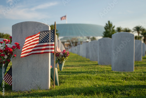 Sarasota National Cemetery with many white headstones with USA flags and flowers on green grass lawn. Memorial Day concept