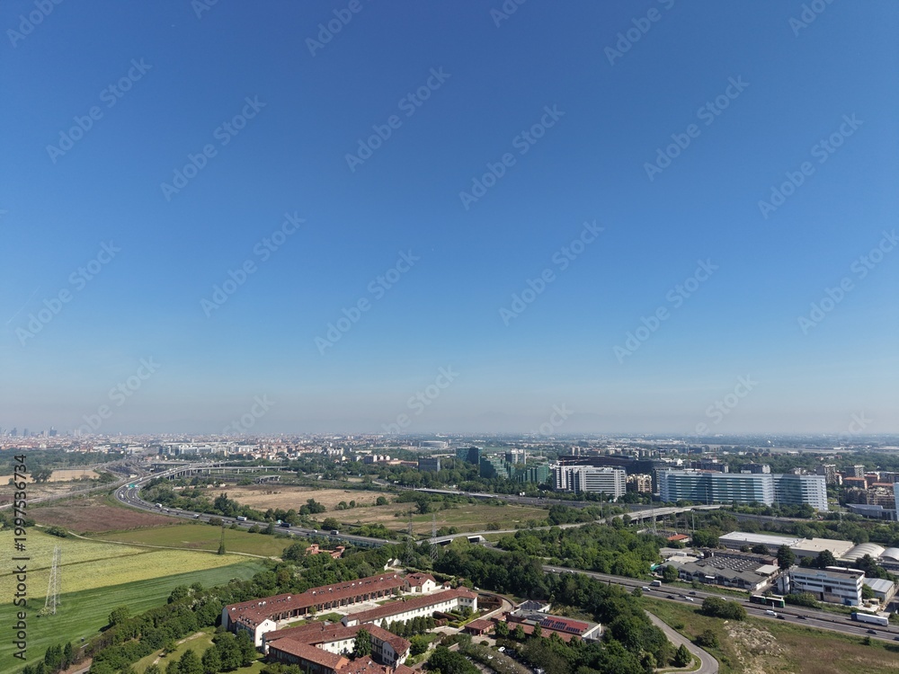 Fototapeta premium A sweeping aerial view of a bustling city stretching towards the horizon under a clear, cloudless sky. Buildings, roads, and green spaces intermingle in a tapestry of urban life.