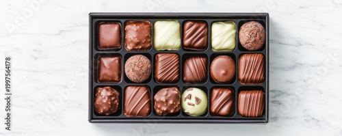 Overhead shot Elegant black box with 18 varied milk, dark and white chocolates, including truffles and pralines, on a luxurious white marble background. Sweet indulgence. Chocolates,