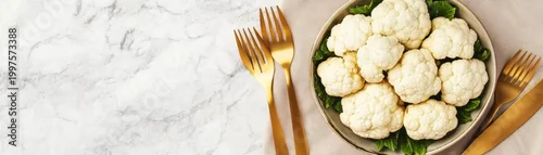 Obraz  z motywem Flat lay of fresh cauliflower florets on green leaves in a bowl, elegantly presented with golden cutlery on a beige napkin and white marble. Healthy dining concept. vegetarian, gourmet