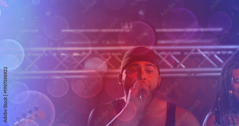 Obraz premium Singing mid-adult singer wearing dark tank top holding mic on concert stage, with truss and bokeh