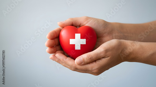 Hands holding a red heart with a white cross symbol representing healthcare and medical care isolated on white background