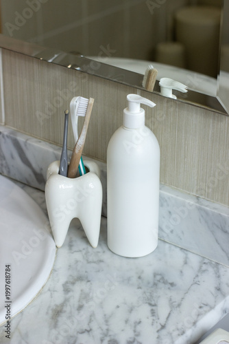 A bathroom countertop with a marble surface, a white soap dispenser, a ceramic toothbrush holder with several toothbrushes.