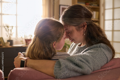 Obraz na płótnie Caucasian mother and daughter embracing closely and touching foreheads on sofa, expressing comfort, trust, emotional support