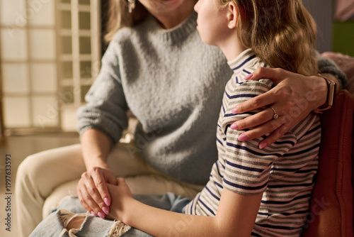 Photography Caucasian mother comforting teenage daughter while holding hands and embracing shoulder during serious home conversation, representing parental support