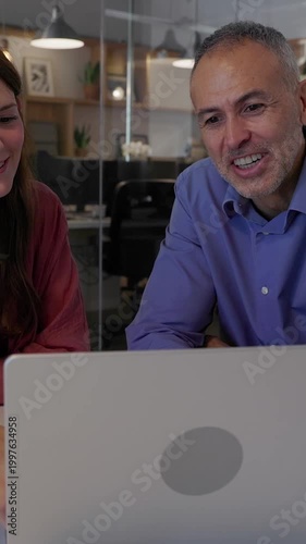 Vertical HD video of manager and colleague working together on a laptop in a meeting room. Two professionals analyzing ideas and coordinating tasks during a focused workplace meeting