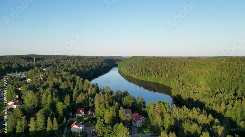 Beautiful aerial perspective of Kaukajärvi in Kangasala, Finland during a clear summer day. The vibrant greens of the forest meet the deep blue lake under bright sunlight, creating a peaceful Nordic
