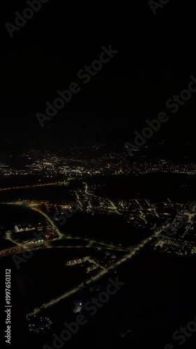 Top down aerial view of bright city lights at night from a landing plane window showing glowing urban streets and dark suburbs.