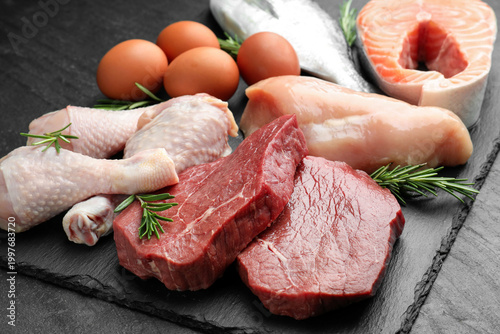Quadro su tela Different types of fresh raw meat, fish, eggs and rosemary on black table, close