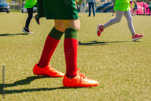 Young girls playing football on a sunny day, wearing bright green jerseys and colorful socks, with a well-maintained artificial turf field in the background