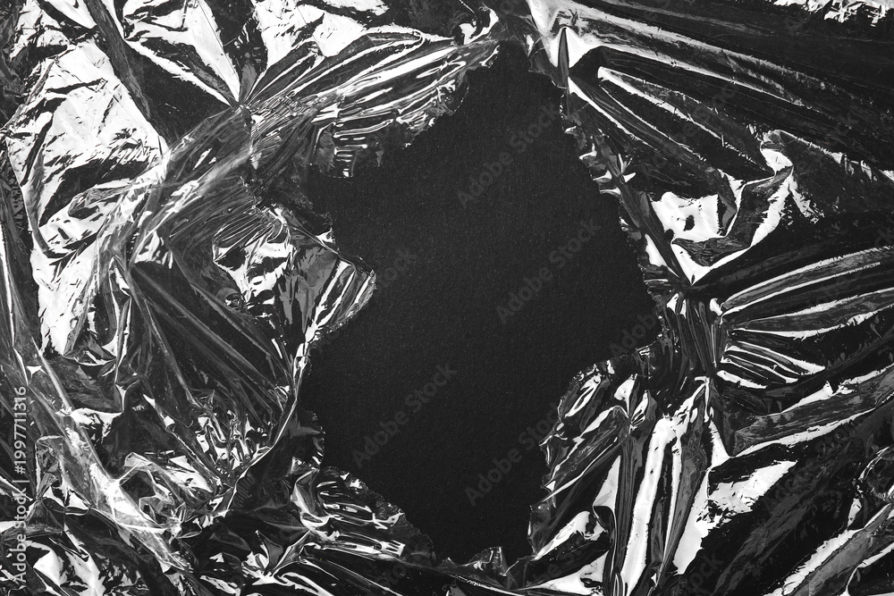 Fototapeta premium Torn plastic wrap on black background, top view. Space for text
