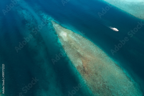 Top-down aerial view of Maldives atolls and reef channels with diving boat navigating turquoise lagoon