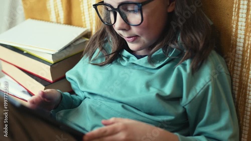 Little Girl in Glasses Using Digital Tablet on Couch with Stack of Books, Child Studying with Pad at Home, 4K 10-bit