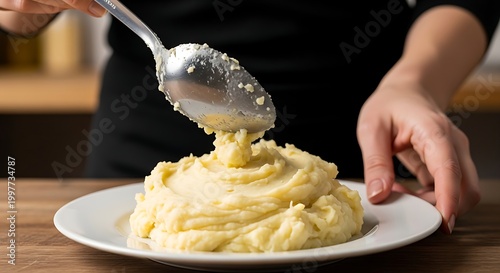 Person serving creamy mashed potatoes on a plate in a kitchen