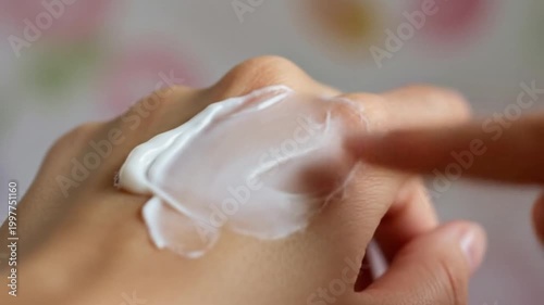 Close up of a person applying white cream to their hand.