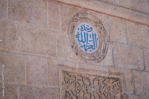 View of intricate blue Arabic calligraphy within a circular medallion on the historic stone walls of Al-Azhar Mosque, Cairo, Egypt.