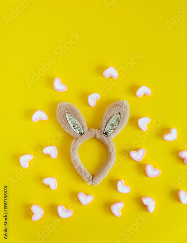 Bunny ears headband surrounded by small heart shapes on a bright yellow background. 