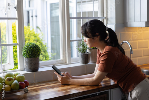 Smartphone resting on wooden countertop beside fruit bowl and potted plants by window, copy space