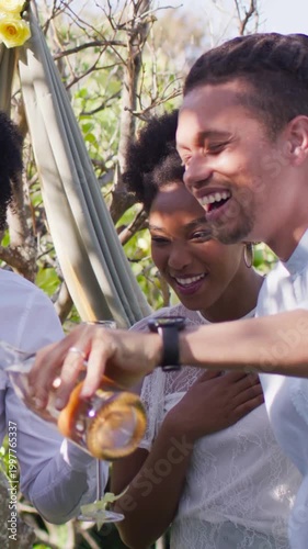 Vertical video: Pouring man tilting bottle, filling glass in garden, woman white-lace celebrating
