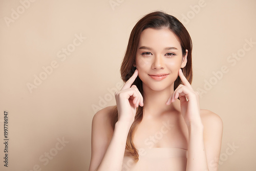 A beautiful young Asian woman with clean, fresh skin against a beige background. Skincare, facial treatment, cosmetology, beauty, and spa. An elegant portrait of an Asian woman.