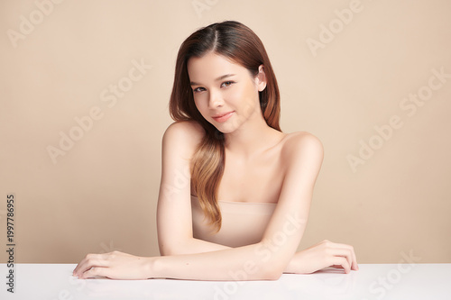 A beautiful young Asian woman with clean, fresh skin against a beige background. Skincare, facial treatment, cosmetology, beauty, and spa. An elegant portrait of an Asian woman.
