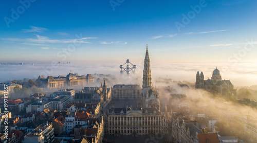 Aerial view of Brussels Grand Place shrouded in morning fog with the Atomium visible in the distance.