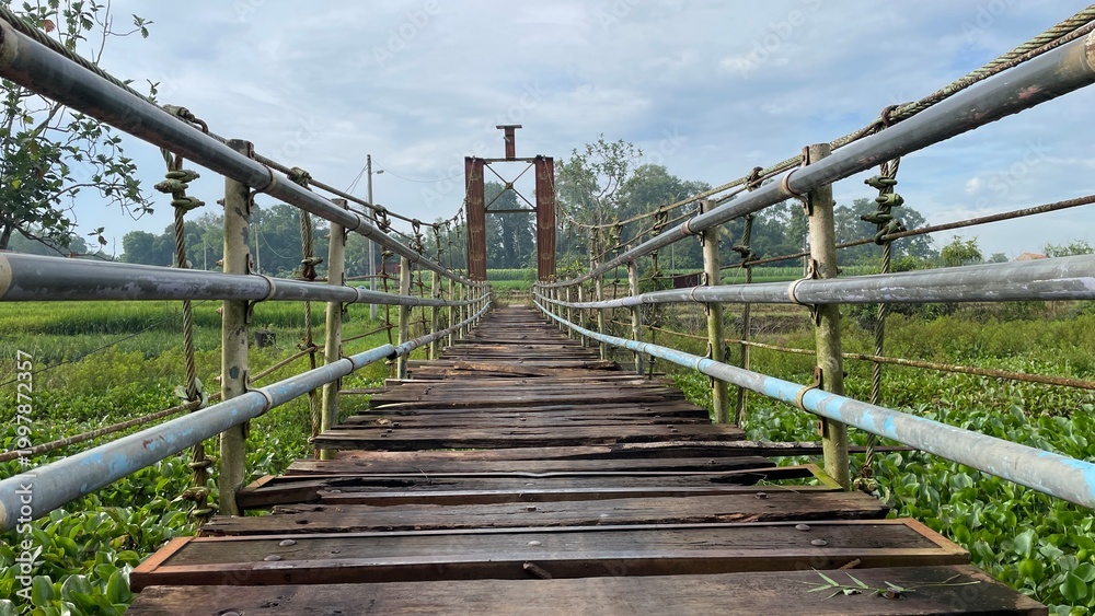 Fototapeta premium Rustic Suspension Bridge Over Water with Wooden Structure and Scenic Natural Landscape View