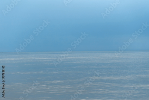 A tranquil minimal seascape of a calm blue ocean meeting a soft pale sky at t...