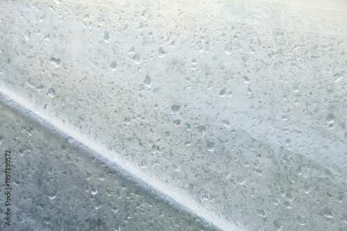 A captivating macro photograph featuring natural morning dew droplets and condensation collected on the surface of a sheet of clear plastic. The image captures the foggy effect created by countless sm