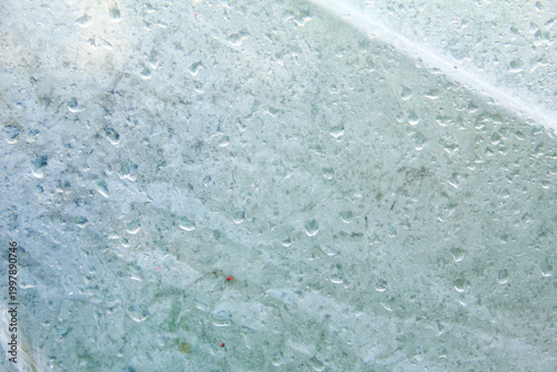 A captivating macro photograph featuring natural morning dew droplets and condensation collected on the surface of a sheet of clear plastic. The image captures the foggy effect created by countless sm