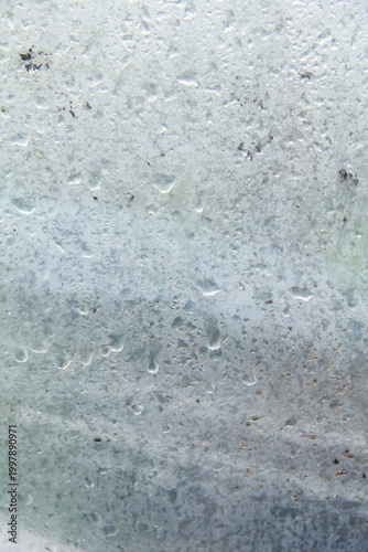 A captivating macro photograph featuring natural morning dew droplets and condensation collected on the surface of a sheet of clear plastic. The image captures the foggy effect created by countless sm