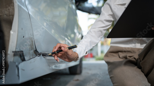 Fotografía Close-up of car accident damage inspection with pen and clipboard, documenting dent and scratches on vehicle body in outdoor parking area