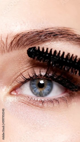Applying black mascara to eyelashes of a beautiful blue eye