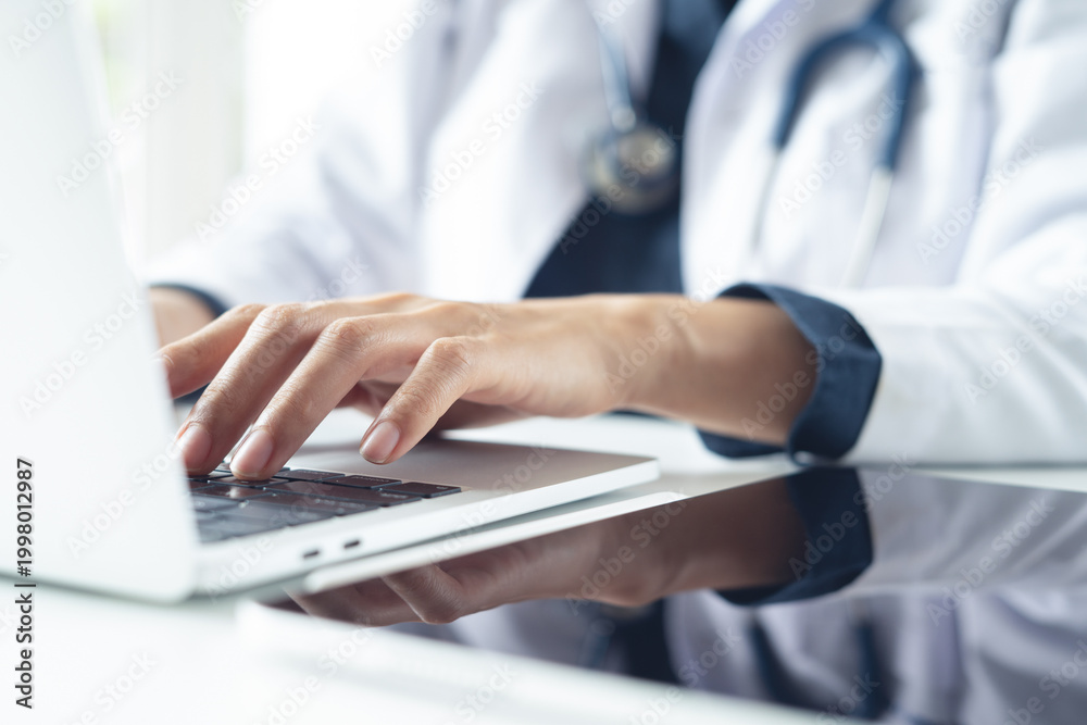 Fototapeta premium Female doctor hands typing on laptop computer in medical office, close up