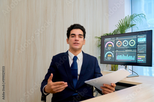 Smart businessman in navy suit present in personal desk with monitor graphic business for business report.