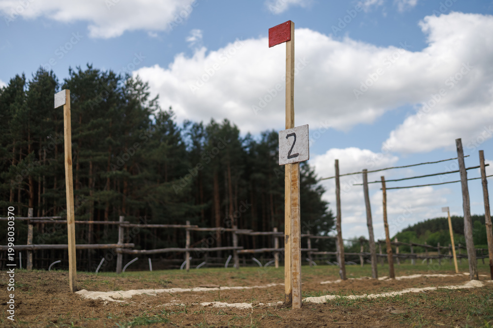 Fototapeta premium Checkpoint number 2 on a wooden pole with a red flag. Training course markings on the ground. Tall pine forest in the background