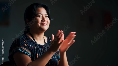 Tracking shot of woman clapping hands and smiling while seated in dimly lit interior studio setting
