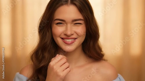 Static close up of woman touching face and smiling in indoor studio with warm golden curtain backdrop