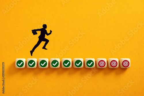 Businessman silhouette leaps across a series of wooden cubes with checkmark icons leading to target symbols as a conceptual metaphor for achieving career goals and success.