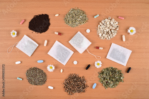 Assortment of dry teas, capsules, tablets, tea bags and daisy flowers on the wooden table. Top view. What to choose: Medicines or herbal treatment?