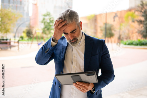 Obraz na plátně Businessman puts his hand to his head upon seeing results on a tablet, feeling s