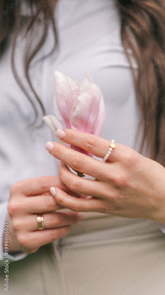 Naklejka premium Woman holding a delicate pink magnolia flower with pearl ring and wedding band