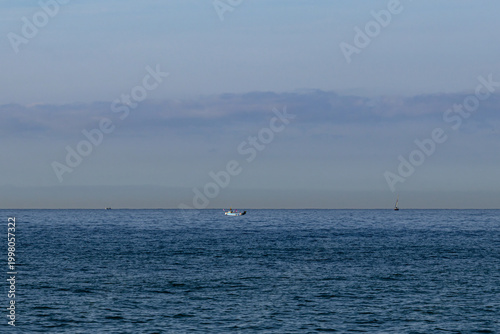 Distant fishing boat sailing on a calm sea horizon under soft blue sky, minimalist marine landscape with peaceful atmosphere and copy space.