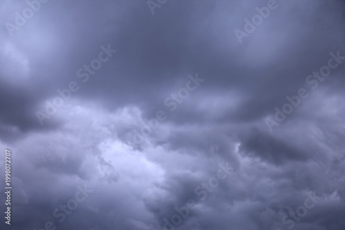 Gray and white turbulent clouds dominate the sky. Low angle perspective looking up on an overcast day. The clouds appear full and heavy, promising rain.
