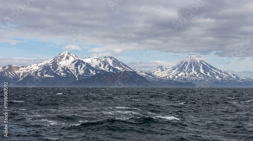 Snow-Capped Volcanoes with Rough Ocean and Cloudy Sky